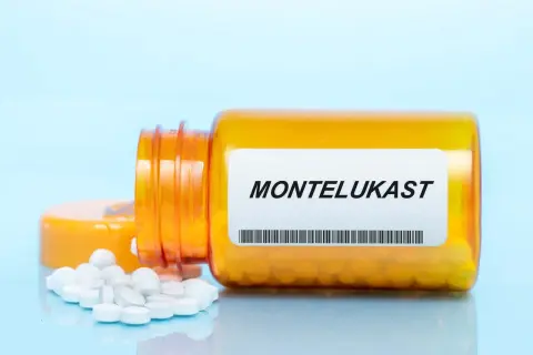 Pomarańczowa butelka leku z etykietą MONTELUKAST, z której wysypały się białe tabletki.