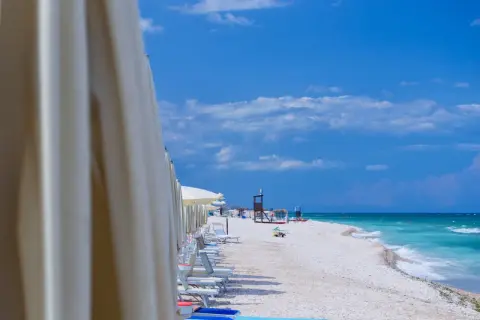 File di ombrelloni bianchi aprono la vista sulla spiaggia di Marotta, con lettini pronti e il mare turchese sotto un cielo azzurro.