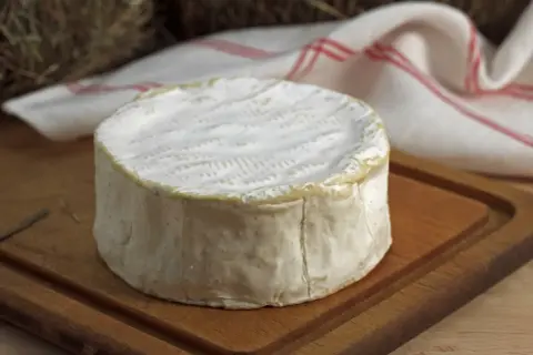 Un delicioso queso francés, con su corteza blanca y cremosa, descansa sobre una tabla de madera.