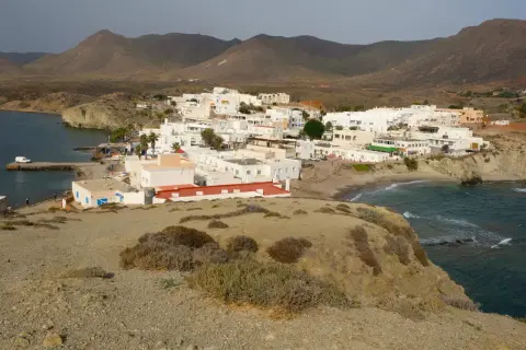 Vista panorámica de la playa Isleta del Moro, con casas blancas, mar azul y montañas áridas al fondo.