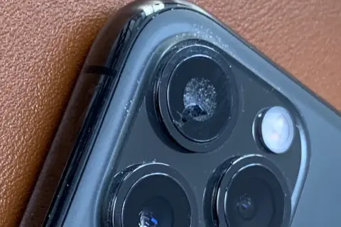 Zbliżenie na pęknięte szkło aparatu iPhone'a na brązowym tle.