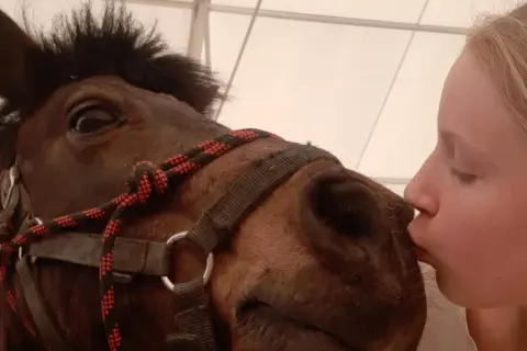 Dziewczynka całuje konia w pysk. To urocze horse play, pełne czułości i radości.