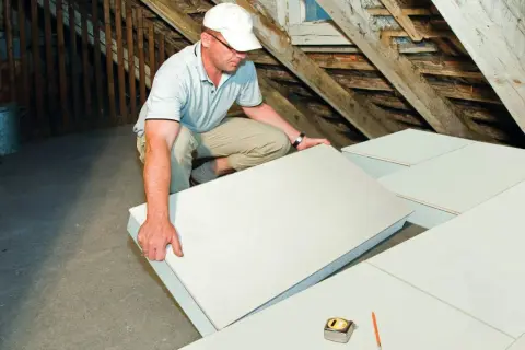 Operaio posa pannelli per isolamento termico in sottotetto. Materiali isolanti edilizia per un tetto efficiente.