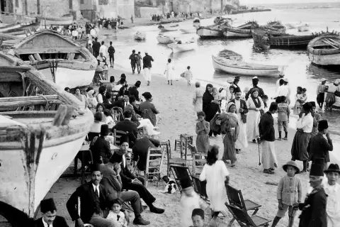Gente en la playa con barcos, un vistazo al posible origen del conflicto entre Israel y Palestina.