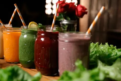 Fem färgglada smoothies i glasburkar, redo för en bebis att njuta av. Grönt, orange, rött och lila.