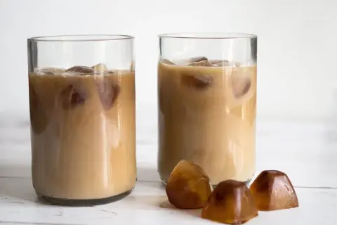 Två glas med iskaffe, perfekt för ett enkelt iskaffe recept. Tre kaffekuber ligger framför.