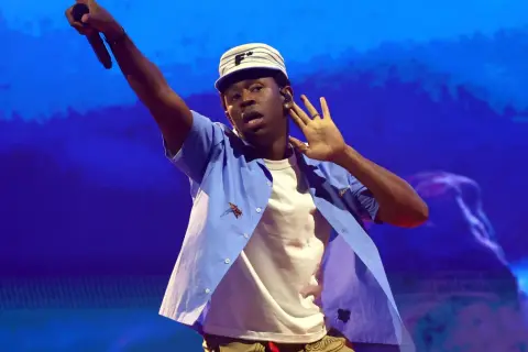 Tyler The Creator w Krakowie, w niebieskiej koszuli i czapce, z mikrofonem w dłoni.