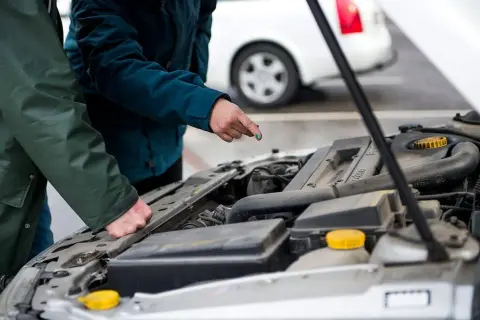 Två personer gör en bil kontroll vid en öppen motorhuv. En pekar på något i motorn.