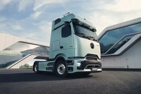 Le dernier camion Mercedes, d'un bleu pâle, est garé devant un bâtiment moderne aux formes courbes et vitrées.