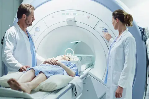 Pacjentka leży w aparacie do rezonansu magnetycznego, a lekarze przygotowują badanie z kontrastem.