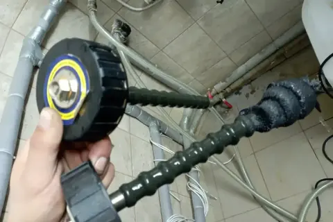 Domowy sposób na czyszczenie instalacji: ręka trzyma narzędzie z okrągłą głowicą, podłączone do elastycznego węża, który prowadzi do rur.