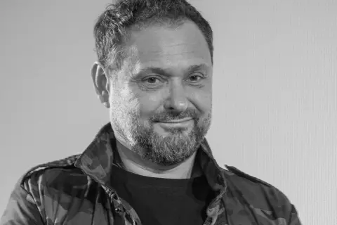 Uśmiechnięty Arkadiusz Tomiak w kurtce moro, z charakterystyczną brodą.