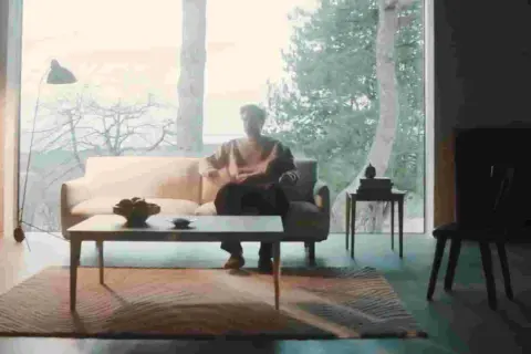 En person sitter i en soffa i ett rum med dansk design inredning. Ett stort fönster visar en vinterskog.