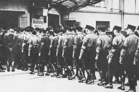Männer in Uniformen marschieren vor dem Reichstag. Die Szene erinnert an die Zeit der deutschen Zentrumspartei, als politische Organisationen eine wichtige Rolle spielten.