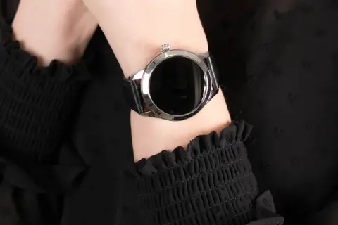 Damski smartwatch z czarnym paskiem na nadgarstku, na tle czarnej bluzki.