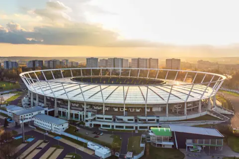 Stadion Śląski w Chorzowie o zachodzie słońca. Obiekt, który gościł niezliczone koncerty, otoczony jest zabudową miejską i zielenią.