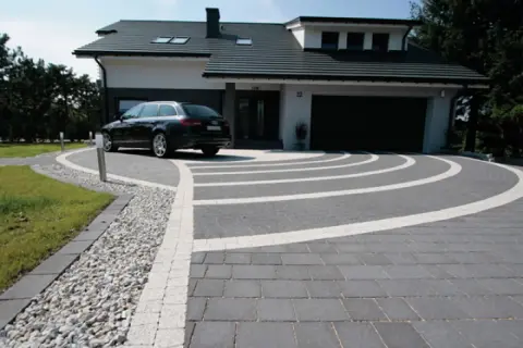 Nowoczesny podjazd z kostki brukowej i żwiru, z eleganckim lany beton na podjazd. Czarny samochód parkuje przed domem.