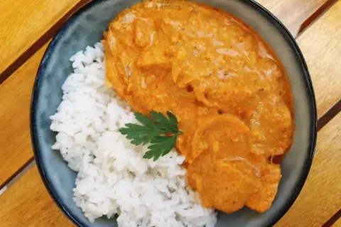 Aksamitny butter chicken w kremowym sosie, podany z ryżem i listkiem pietruszki. Pyszne danie na drewnianym stole.