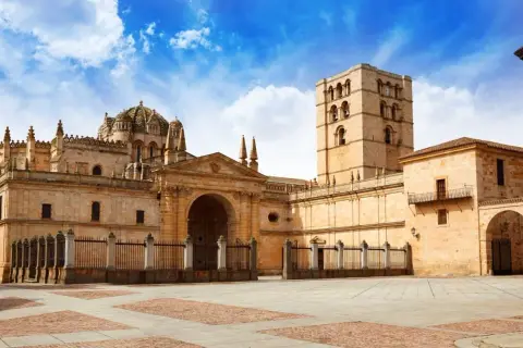 Imponente catedral románica en España, con su torre campanario y cúpula, bajo un cielo azul con nubes.