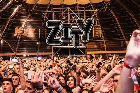 Multitud animada en la entrada del espacio Zity, con brazos en alto y móviles grabando el evento.