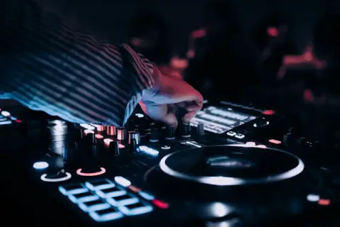 Dłoń DJ-a regulująca pokrętła na konsoli, w tle rozmyte światła.