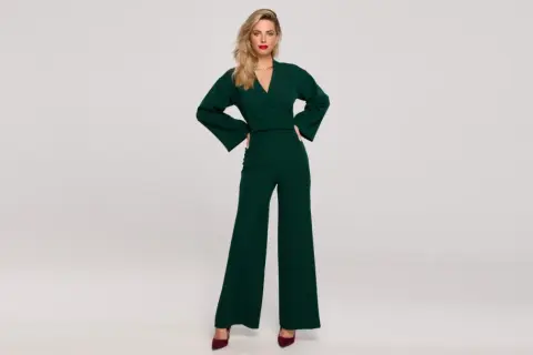Elegancka kobieta w zielonym kombinezonie z szerokimi nogawkami. Góra z kopertowym dekoltem i bufiastymi rękawami. Idealny wybór, co na górę do kombinezonu.
