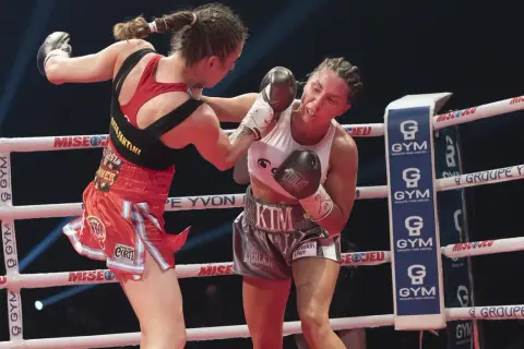 Two female boxers in a strawweight boxing match exchange punches in the ring. One boxer lands a blow to the other's face.