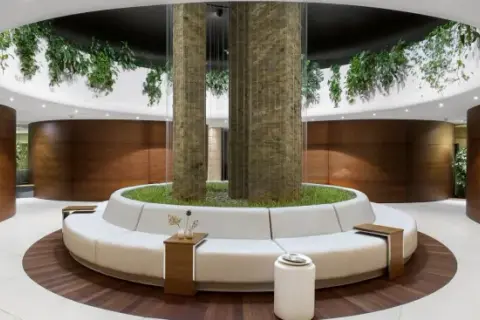 Nowoczesne wnętrze spa z okrągłą sofą, roślinnością i drewnianymi panelami.