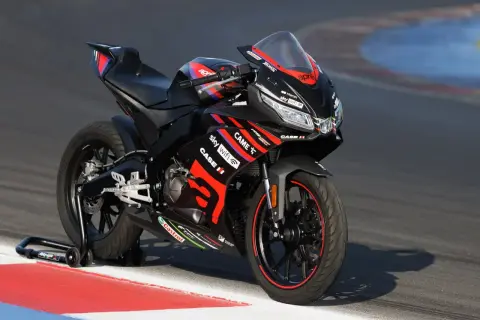 Czarny motocykl Aprilia 125 na torze wyścigowym. Zastanawiasz się, ile jedzie motor 125? Ten sportowy model jest gotowy do akcji.