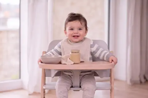 Ein lächelndes Baby sitzt im Hochstuhl, bereit für Brei. Was kann ein Baby mit 9 Monaten? Es kann schon viel, wie dieses fröhliche Kind beweist!