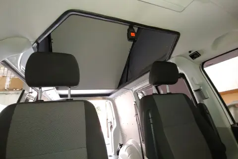 Interior de furgoneta con asientos delanteros y un techo elevable abierto, listo para la aventura.