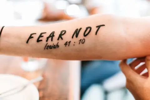 Tatuaż a religia: napis "FEAR NOT" z cytatem z Izajasza 41:10 na przedramieniu.