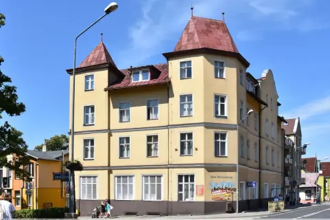 Żółta kamienica w Międzyzdrojach, z banerem "Delfin Międzyzdroje Cennik" i reklamą "Delfin Domowe Obiady".