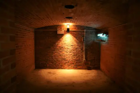Interior de sótano de ladrillo con luz cálida y una lámpara fluorescente.