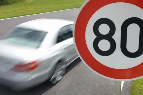 Znak ograniczenia prędkości do 80 km/h. Biały samochód pędzi po drodze, przypominając o przepisach ruchu drogowego i ograniczeniach prędkości w Polsce.