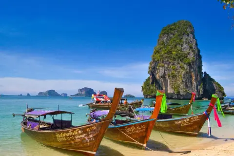 Träbåtar guppar i det turkosa vattnet vid Koh Hong. En imponerande klippa reser sig ur havet.