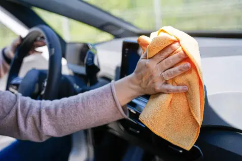 Mano limpiando el salpicadero del coche con un paño naranja. Descubre trucos caseros para limpiar el salpicadero del coche y mantenerlo impecable.