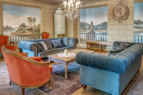 Elegancki salon w hotelu 5 gwiazdkowym. Miękkie sofy, aksamitne fotele i zabytkowy piec tworzą przytulną atmosferę.