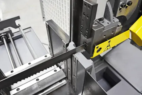 Precyzyjne cięcie drewna dzięki odpowiedniej prędkości piły taśmowej. Widoczna taśma tnąca i mechanizm prowadzący.