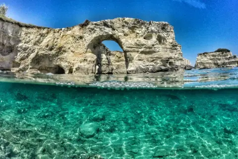 Arco naturale e faraglioni nel mare cristallino del Salento, il mare più bello. Acqua turchese e rocce bianche sotto un cielo azzurro.