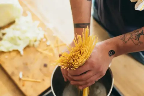 Hände mit Tattoos halten Spaghetti über einen Topf. Das bedeutet al dente: perfekt gekochte Pasta.