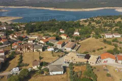 Vista aérea de Cervera de Buitrago, con casas de tejados naranjas y un embalse azul al fondo.