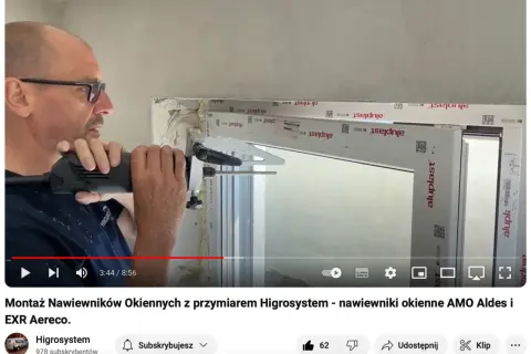 Montaż nawiewnika w oknie. Mężczyzna wierci otwór w ramie okiennej, przygotowując miejsce na nawiewnik.