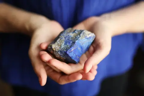 Manos sostienen un trozo de lapislázuli, su intenso azul resalta contra la tela azul.
