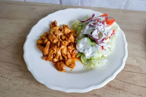 Talerz z porcją pikantnego kurczaka i świeżą sałatką z pomidorów, ogórka i cebuli. Tak wygląda shoarma co to za danie!