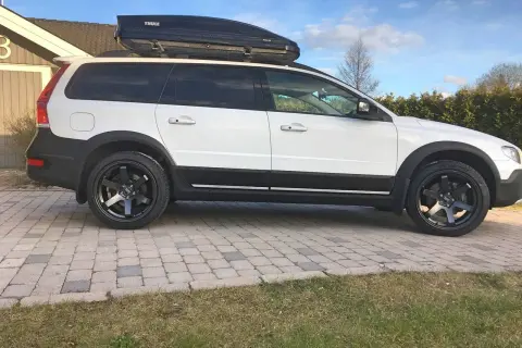 Vit Volvo XC70 2016 med takbox och svarta fälgar. Kanske ett problem med att få plats med allt bagage?