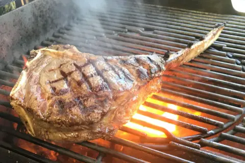Ein saftiges Tomahawk Steak grillen, mit sichtbaren Grillstreifen und Flammen darunter.