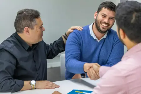 Hombres estrechando manos y sonriendo. Uno pone una mano en el hombro del otro, como si cerraran un trato importante, quizás sobre cómo es obligatorio tener seguro de hogar.