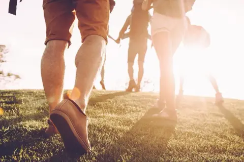 Des randonneurs marchent sur une colline herbeuse au coucher du soleil. Une façon naturelle de muscler son dos en marchant.