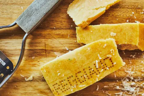 Des morceaux de **croûte parmesan comestible** sur une planche en bois, avec un râpe à fromage.